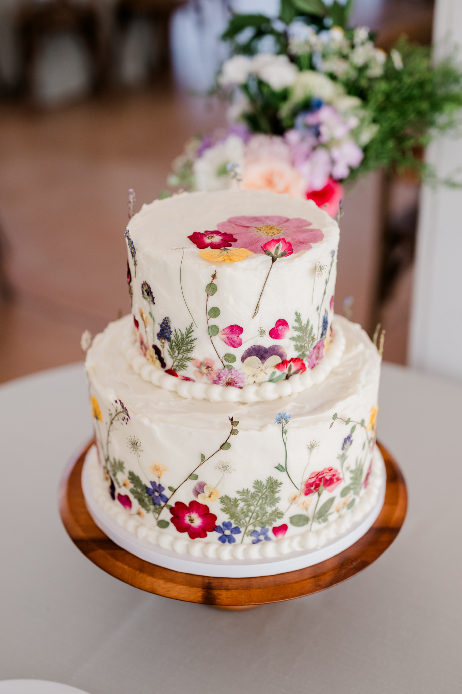 A wedding cake with cream cheese frosting decorated with pressed flowers.